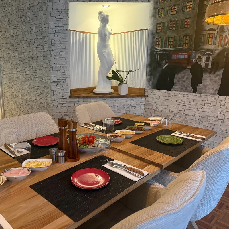 Gedeckter Holztisch mit Stühlen, Statue und Wandgemälde im Gastraum