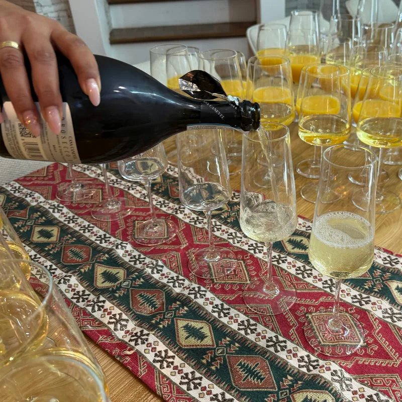 Eine Hand schenkt Schaumwein in ein Glas neben vorbereiteten Gläsern