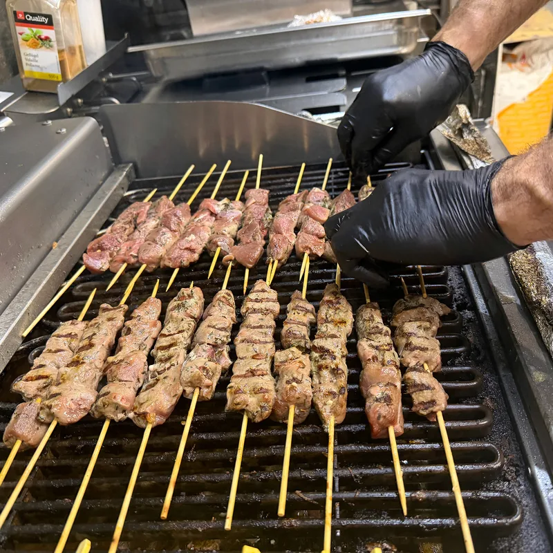 Hände in schwarzen Handschuhen wenden Fleischspiesse auf dem Grill