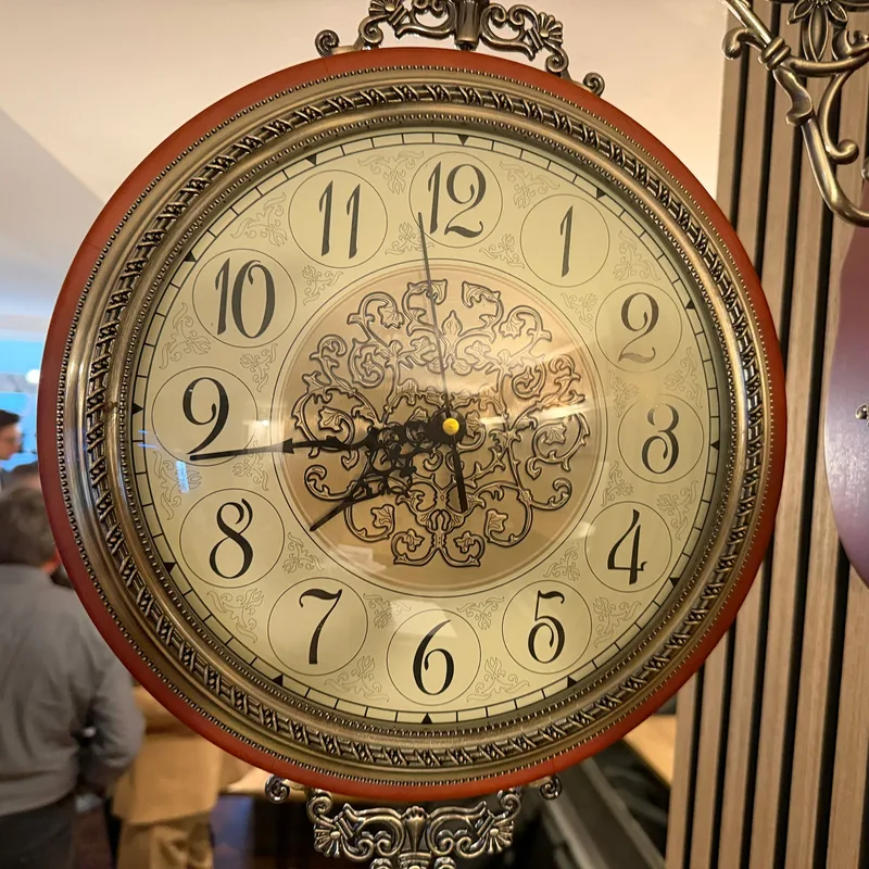 Grosse verzierte Standuhr mit Zifferblatt vor Gästen im Lokal