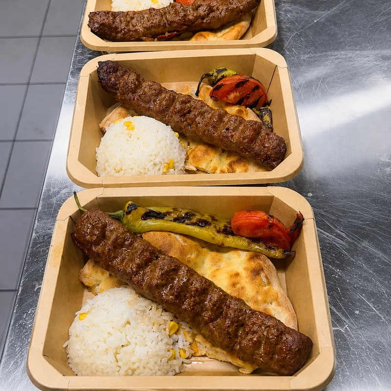 Adana-Kebab in Boxen zum Mitnehmen, mit Reis, Fladenbrot und Grillgemüse